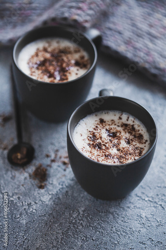 Two cups of hot cocoa with chocolate on grey background