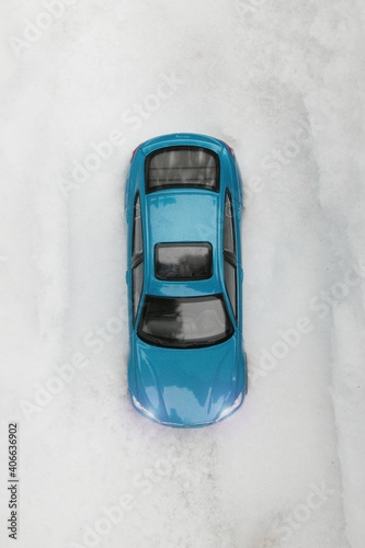 Bird`s eye view of blue passenger car in deep snow.A blue passenger car without a driver stands on the road in deep snow. The road is not visible through the snow. © luckakcul