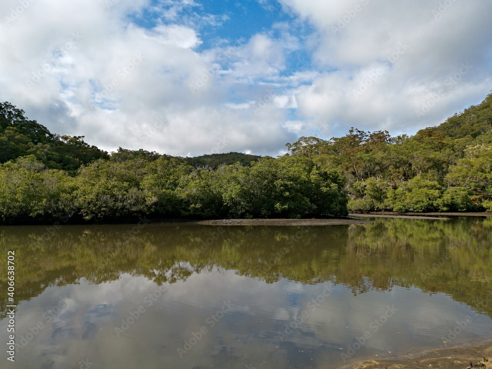 Beautiful morning view of a creek with reflections of deep blue sky, light clouds, mountains and trees, Cockle Creek, Bobbin Head, Ku-ring-gai Chase National Park, New South Wales, Australia
