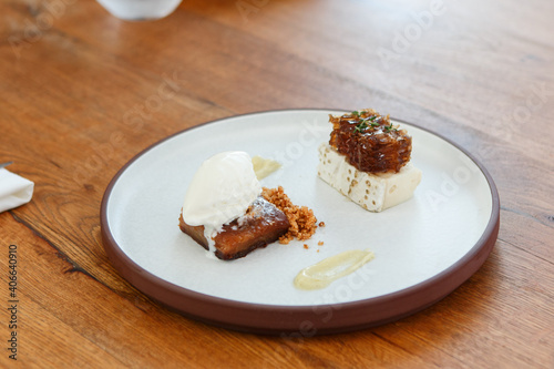 Gourmet dessert, including a honey cake, goat cheese and a honeycomb, served on a flat round stoneware plate with a tall rim.