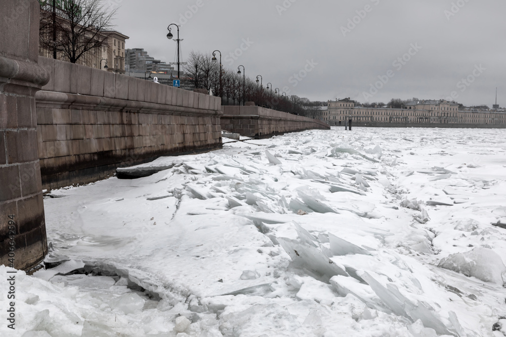 Obraz premium Snowy frozen river with a beautiful old stone embankment. Chunks of ice on the water. Cloudy winter day. 