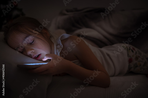 A cute little girl fell asleep on a pillow with a phone in her hand.