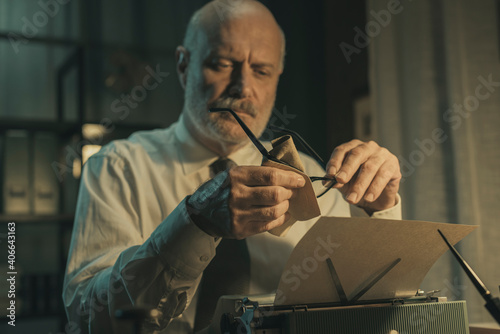 Businessman sitting at desk and cleaning his glasses