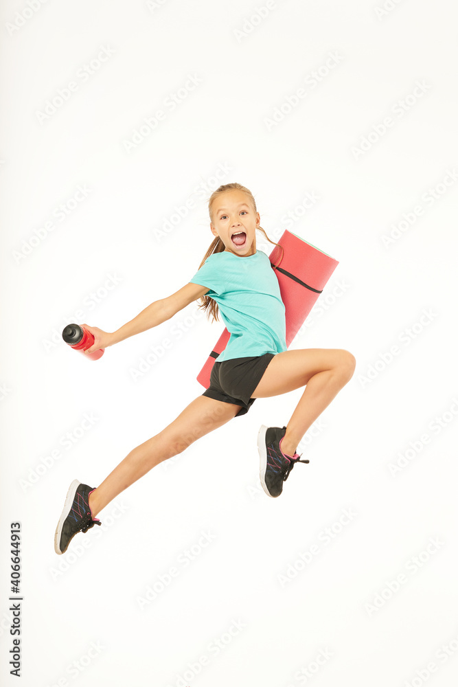 Cute girl with yoga mat and bottle of water jumping and screaming