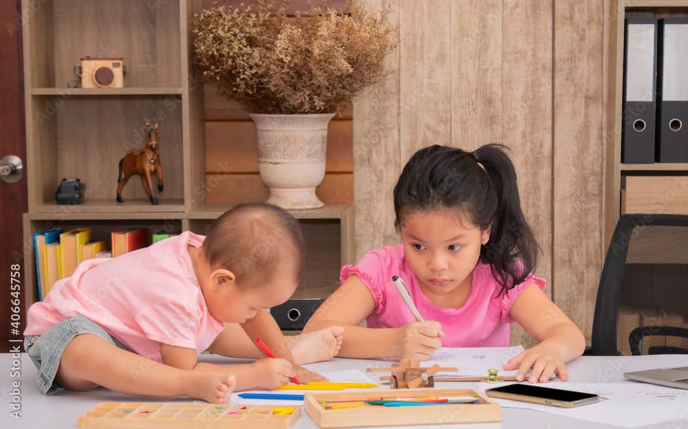 Adorable 2 kids sitting on desk full of crayon colors and white papers enjoy playing together at home, 2 sibling happy drawing with their imagination, elder sister play with naughty younger sister Adorable 2 kids sitting on desk full of crayon colors and white papers enjoy playing together at home, 2 sibling happy drawing with their imagination, elder sister play with naughty younger sister