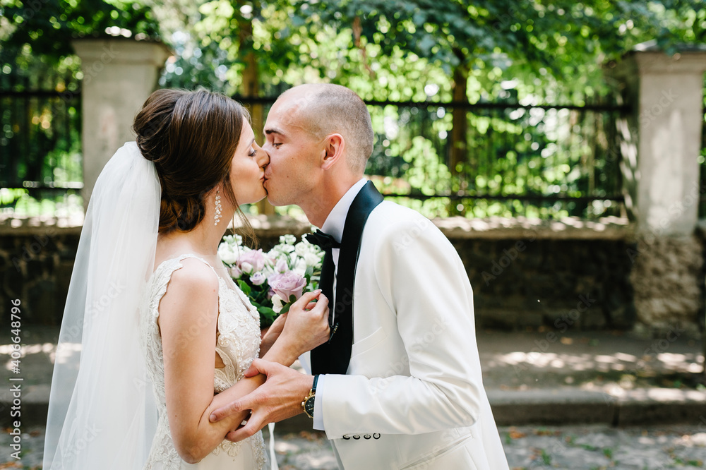 The first meeting is newlyweds in a green park outdoors. Bride kissing groom, surprise in nature. Happy wedding day of marriage. The first meeting is newlyweds in a green park outdoors. Bride kissing groom, surprise in nature. Happy wedding day of marriage.