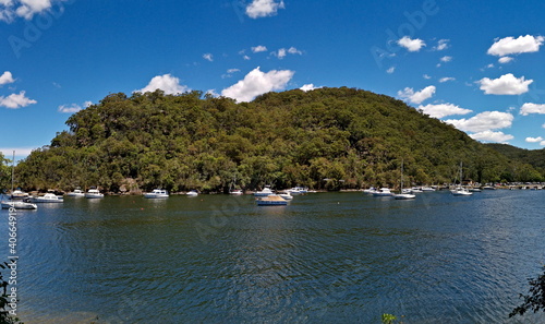 Beautiful panoramic view of a creek with boats, mountains, trees, blue sky with light clouds in the background, Bobbin Head, Ku-ring-gai Chase National Park, New South Wales, Australia 