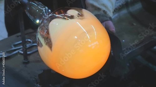 Glass blower forming hot piece of glass with wooden tool. Traditional glass crafter works with  burning and blowing an art piece. Hand made glass studio in Kunratice.