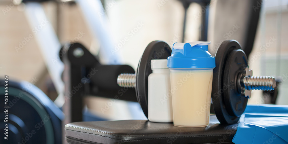 Fototapeta premium Protein sports shake, elastic tape and dumbbells in the home gym.