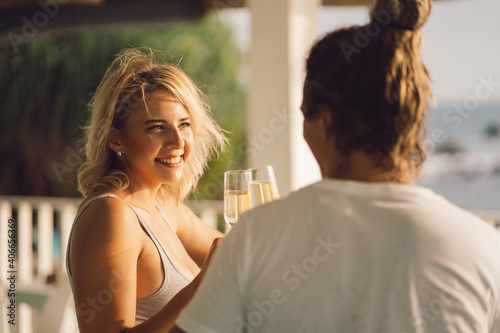 Romantic couple in a cafe at sunset drinks wine. The girls face looks at the man, the man from the back. Happy girl with blond hair on the background of the ocean.