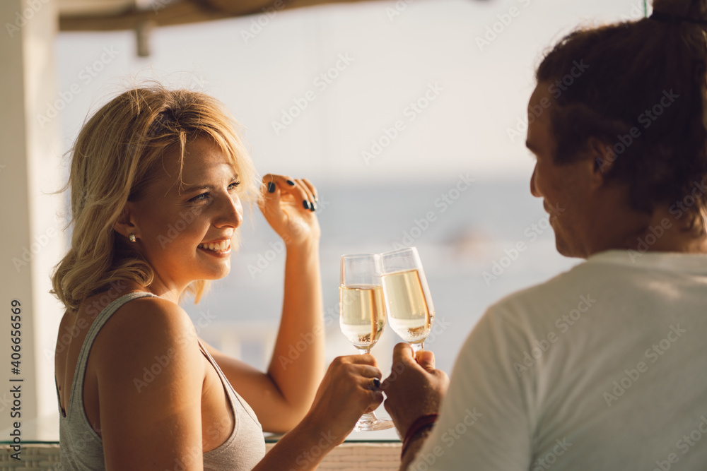 Romantic couple in a cafe at sunset drinks wine. The girls face looks at the man, the man from the back. Happy girl with blond hair on the background of the ocean. Romantic couple in a cafe at sunset drinks wine. The girls face looks at the man, the man from the back. Happy girl with blond hair on the background of the ocean.