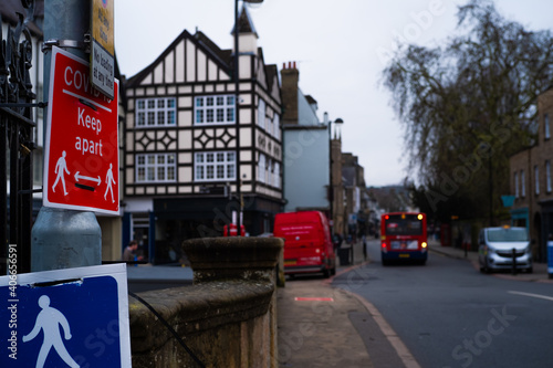 Red sign on a post related to Covid19, saying to keep 2 meters apart. Public bus in the background out of focus, concepts of covid and public transport in the UK. Bridge in the Cambridge city center photo