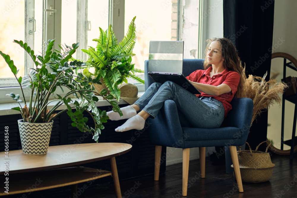 Young female using laptop after work, communicates on Internet with customer. Happy freelance woman is relaxing on comfortable couch and using laptop at home. Young female using laptop after work, communicates on Internet with customer. Happy freelance woman is relaxing on comfortable couch and using laptop at home.