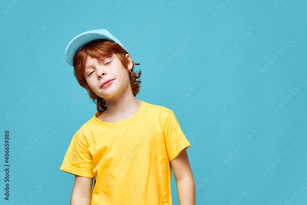 Red-haired boy eyes closed tilting his head to one side yellow t-shirt cap studio Red-haired boy eyes closed tilting his head to one side yellow t-shirt cap studio