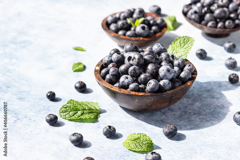 Freshly picked juicy blueberries in wooden bowl with mint on blue background. Antioxidant. Concept for healthy eating and nutrition. Bright light and trendy shadows.