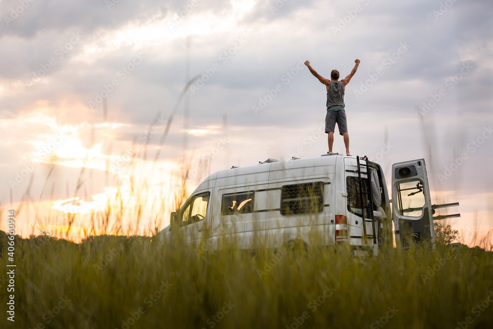 Man with raised arms on top of his camper van - obrazy, fototapety, plakaty 