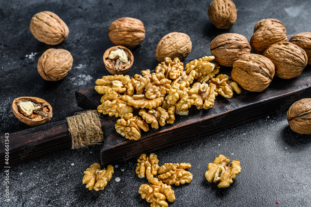 Shelled walnuts kernels on wooden cutting board. Black background. Top view