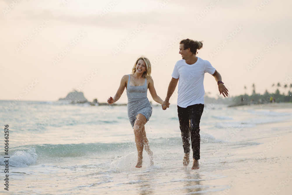 Happy couple of man and woman run along the shore holding hands.