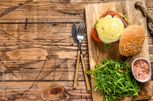 Big sandwich  burger with beef, tomato, cheese and arugula.  wooden background. Top view. Copy space