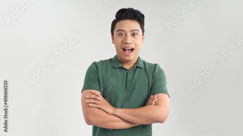 Happy young man. Portrait of handsome young man keeping arms crossed and smiling while standing against grey background