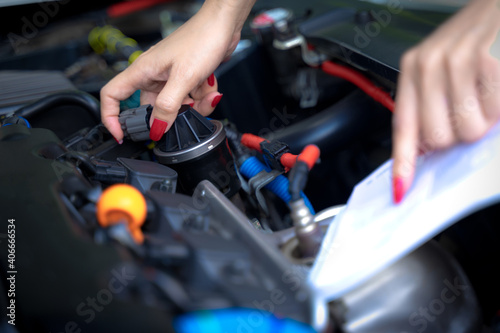 A woman fixes her car and opens a car manual to fix her car on a non-start day © TEEREXZ