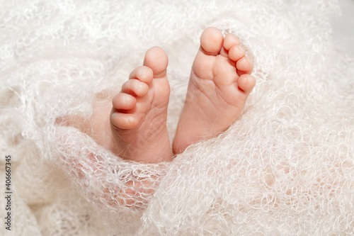 Detail of a newborn baby feet with soft white blanket. Close up picture of new born baby feet on knitted plaid