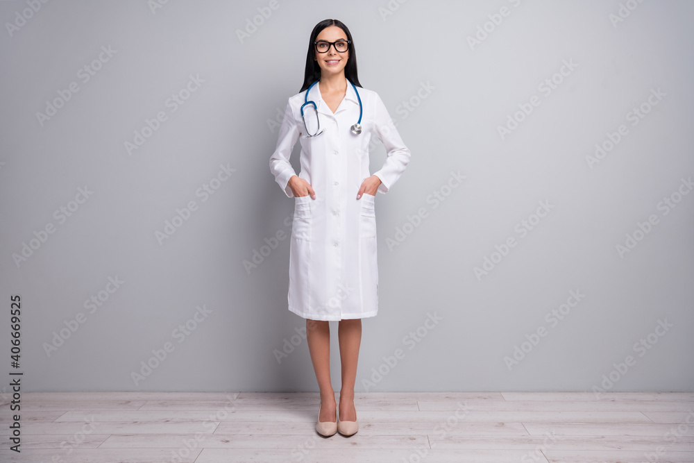 Full length photo of doctor lady hands pockets wear eyewear stethoscope white uniform isolated grey color background Full length photo of doctor lady hands pockets wear eyewear stethoscope white uniform isolated grey color background