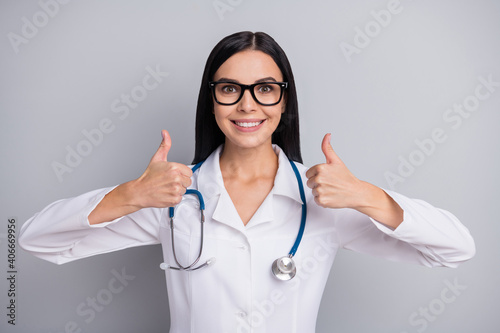Photo of doctor girl raise two hands show thumbs up wear specs stethoscope white uniform isolated grey color background