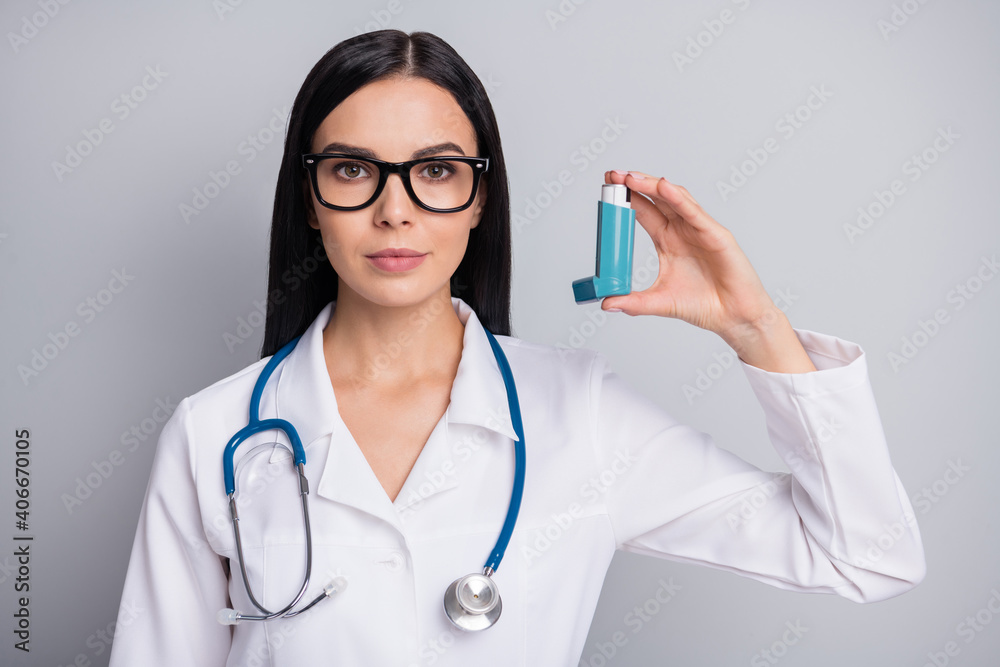 Photo of serious confident lady doctor wear white coat eyeglasses holding respiratory inhaler isolated grey color background Photo of serious confident lady doctor wear white coat eyeglasses holding respiratory inhaler isolated grey color background