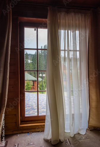 Large floor to ceiling partly curtained wooden window  inside view