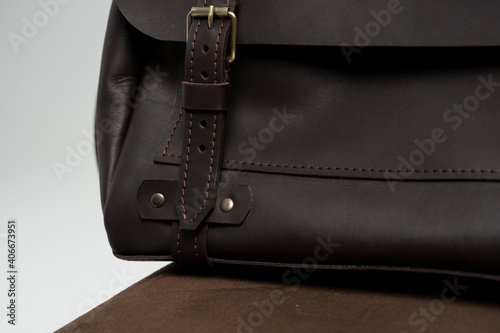 Details of brown men's shoulder leather bag for a documents and laptop on a brown chair with a white background. Mens leather brief case, messenger bags, leather satchel, handmade briefcase.