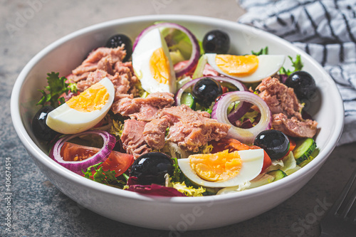 Tuna salad with egg, olives and vegetables in white bowl, dark background. Diet food concept.