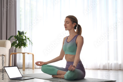 Woman having online video class via laptop at home. Distance yoga course during coronavirus pandemic