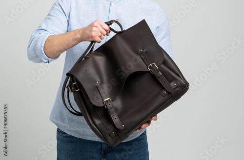 Brown men's shoulder leather bag for a documents and laptop on the shoulders of a man in a blue shirt and jeans with a white background. Satchel, mens leather handmade briefcase.