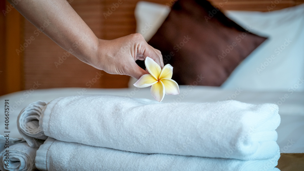 Hands of hotel maid putting plumeria flower and towels on the bed in the luxury hotel room ready for tourist travel Hands of hotel maid putting plumeria flower and towels on the bed in the luxury hotel room ready for tourist travel