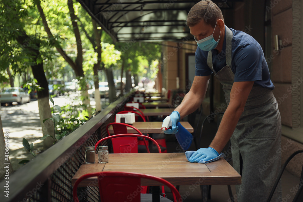 Waiter in mask and gloves disinfecting table at outdoor cafe Waiter in mask and gloves disinfecting table at outdoor cafe
