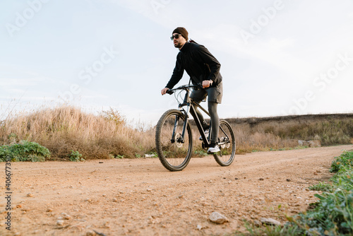 Handsome unshaven guy in sunglasses riding his bicycle outdoors