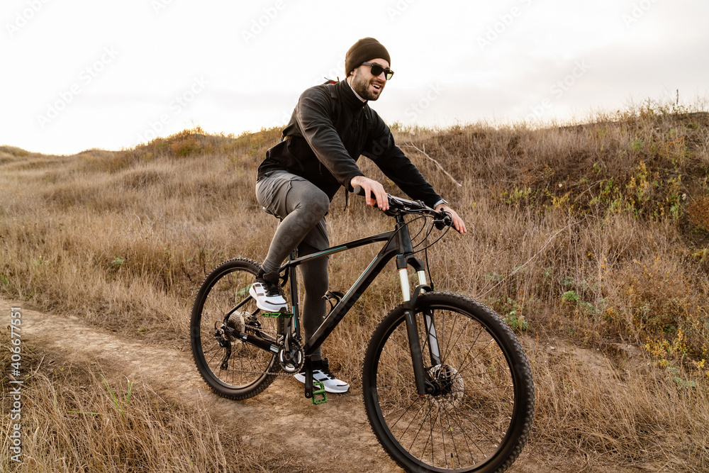 Happy unshaven guy in sunglasses riding his bicycle outdoors