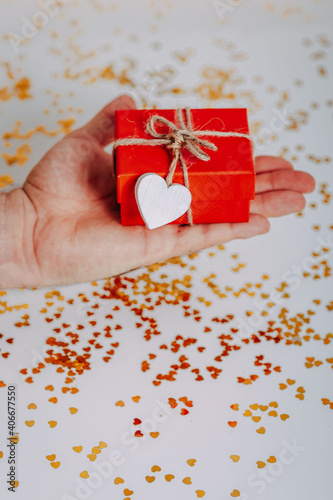 Obraz na płótnie Man heand with small red gift box with golden glitters around. Red present with heart on the rope on white background. Saint Valentine's Day present. Heart-shaped golden glitters. w salonie
