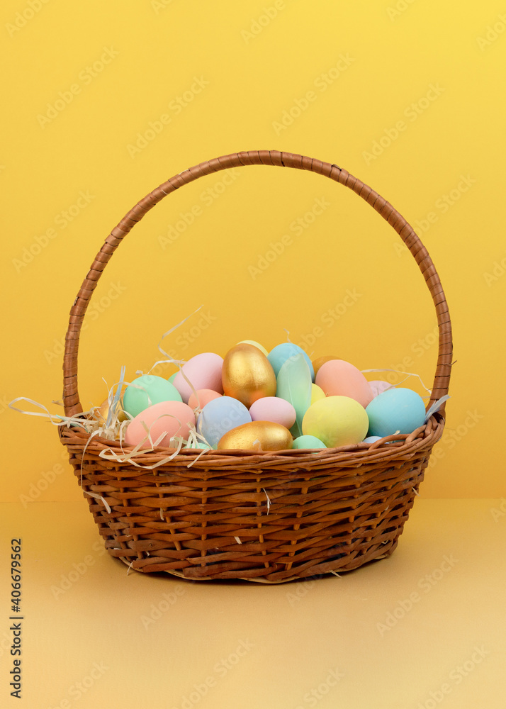 Wicker basket with colorful Easter eggs in pastel colors on yellow background