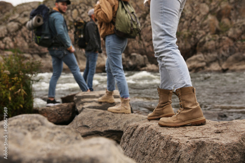 Group of friends with backpacks crossing mountain river  focus on hiking boots