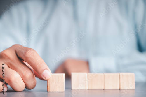 Businessman wearing a blue shirt, arranging the empty wooden blocks with his hands. Which is placed on a white wooden table. Business strategy and action plan. Copy space.