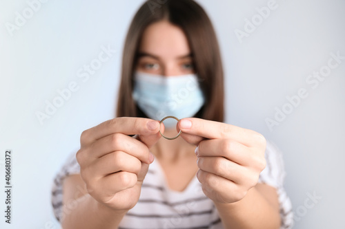 Woman in protective mask holding wedding ring against light background  focus on hands. Divorce during coronavirus quarantine