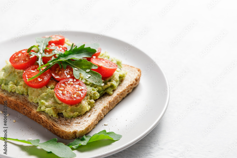 Avocado rye bread toast with cherry tomatoes and arugula on bright background, healthy vegan sandwich.