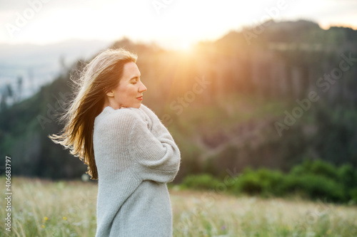 Happy woman enjoying stay on the green grass on the forest peak of mountain. Fresh air, Travel, Summer, Holidays, Journey, Trip, Lifestyle. Health care, authenticity, sense of balance and calmness. 