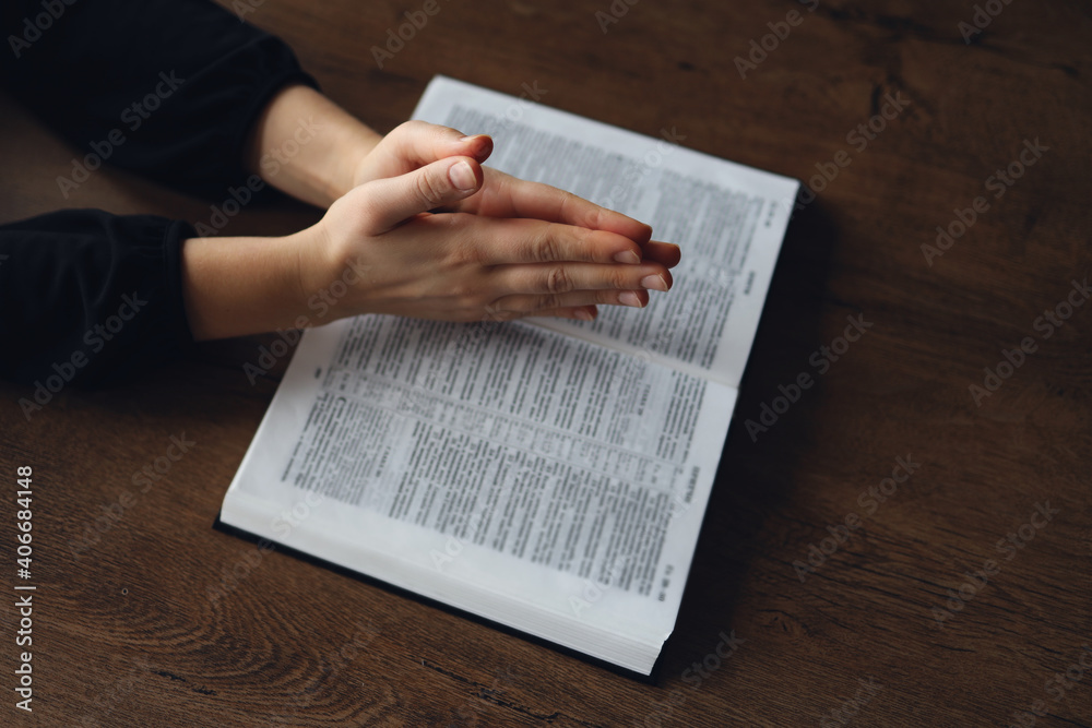Woman hands on Bible. she is reading and praying over bible in a dark space over wooden table Woman hands on Bible. she is reading and praying over bible in a dark space over wooden table