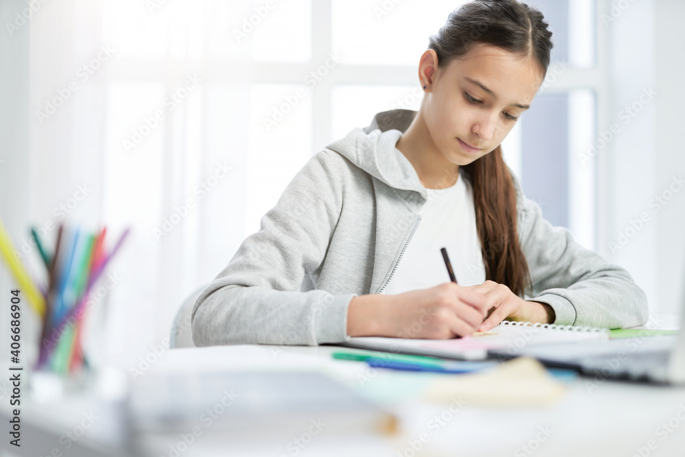Studying matters. Concentrated latin teenage girl making notes in her copybook while doing homework, sitting at the table at home Studying matters. Concentrated latin teenage girl making notes in her copybook while doing homework, sitting at the table at home