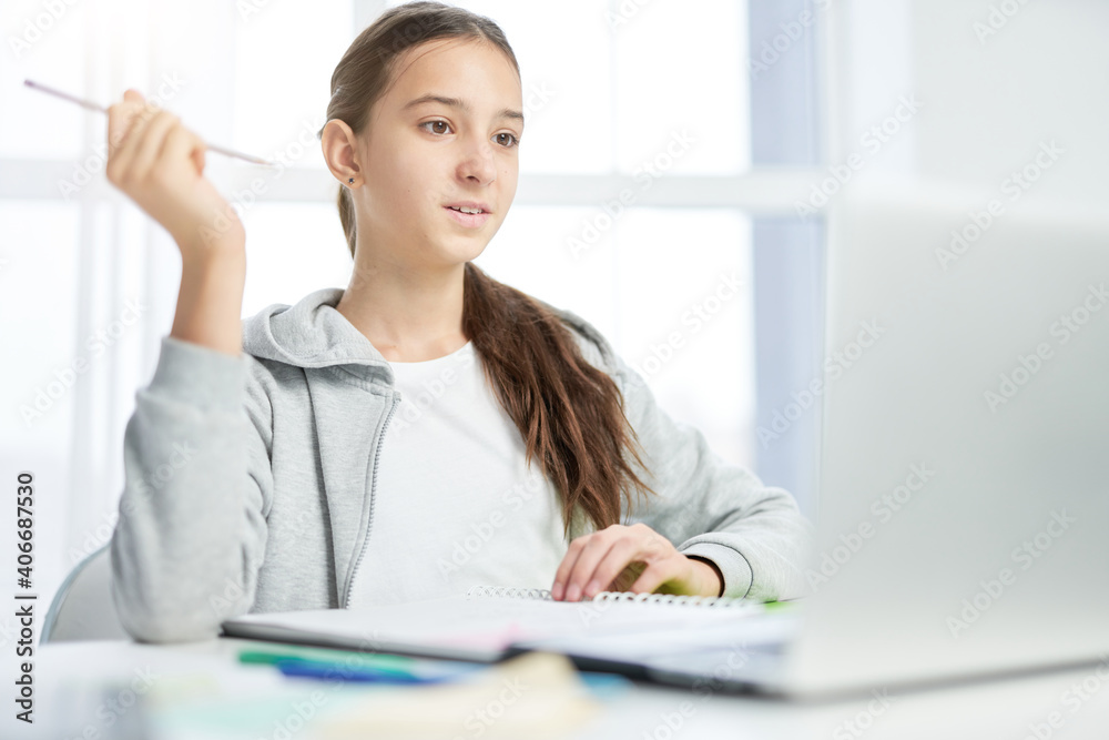 Pretty latin teenage girl looking at the screen of laptop while communicating with her teacher, having online lesson at home Pretty latin teenage girl looking at the screen of laptop while communicating with her teacher, having online lesson at home