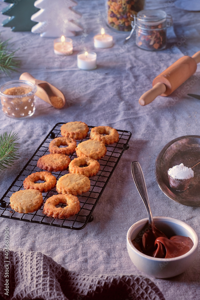 Sandwich cookies filled with hazelnut spread, nougat cream. Christmas Linzer cookies filled on cooling rack, metal plate. Winter decor, linen tablecloth. Sandwich cookies filled with hazelnut spread, nougat cream. Christmas Linzer cookies filled on cooling rack, metal plate. Winter decor, linen tablecloth.