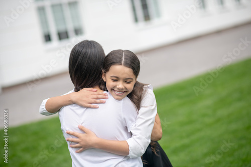Daughter hugging tightly mom in the schoolyard